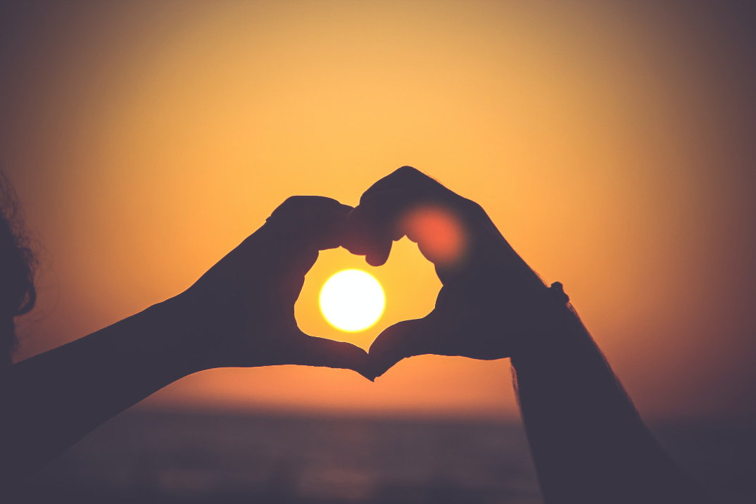 Hände formen ein Herz bei Sonnenuntergang