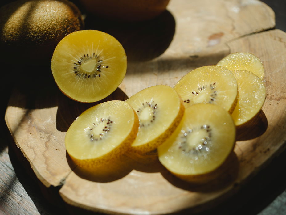 Eine aufgeschnittene, gelbe Kiwi auf einem Holzbrett.
