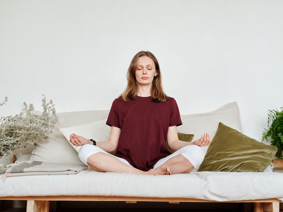 Eine Frau meditiert auf dem Sofa.