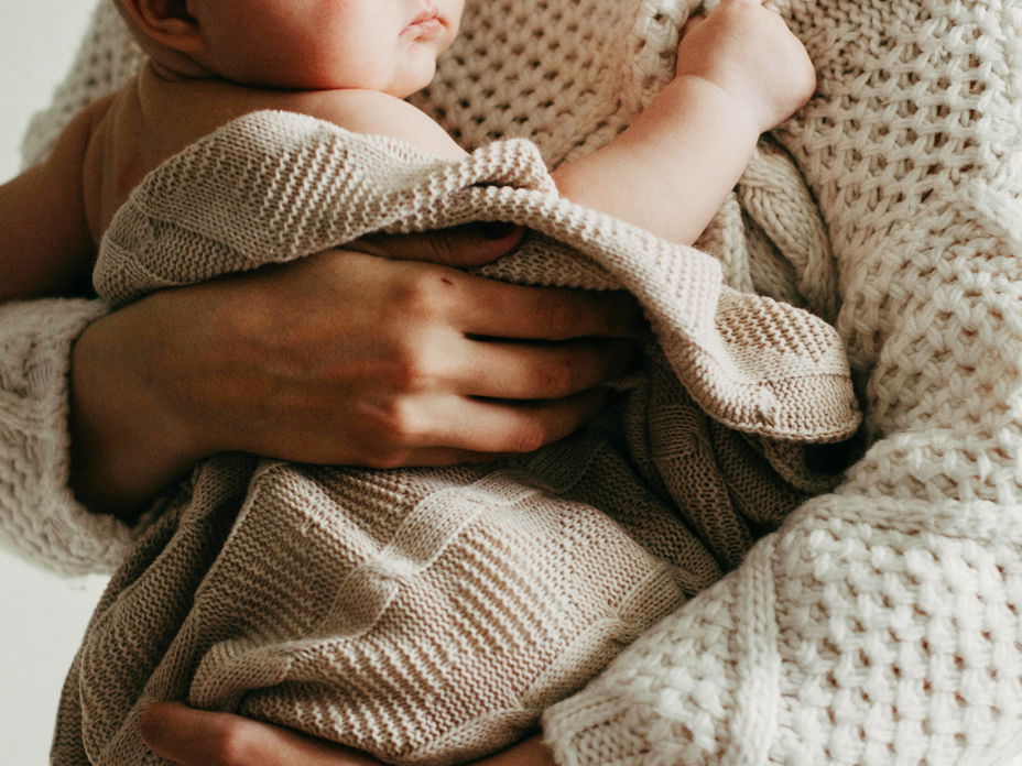 Frau hält ein Baby, das in eine Decke gehüllt ist.