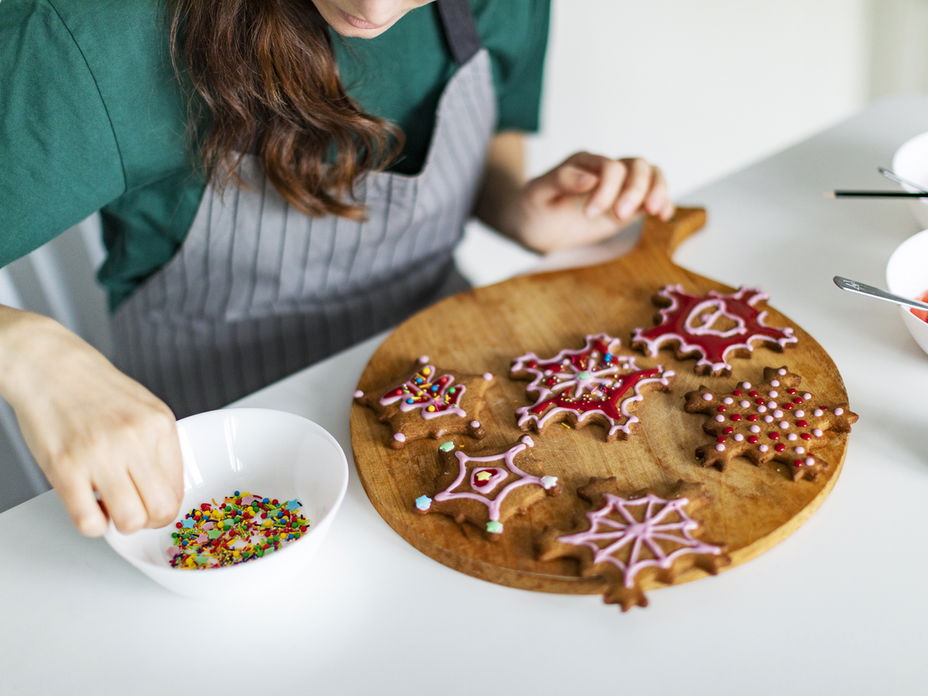 Frau verziert weihnachtliche Plätzchen mit Zuckerguss und bunten Streuseln.