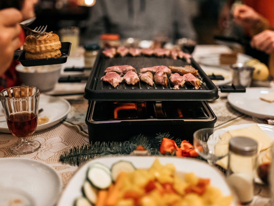 Ein Raclette-Gerät steht auf einer festlich gedeckten Tafel.