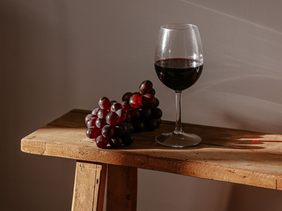 Ein Glas Rotwein und Trauben auf einer Holzbank.