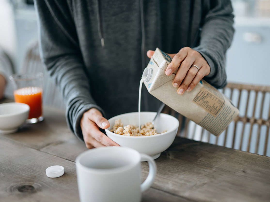 Frau gießt sich Hafermilch ins Müsli