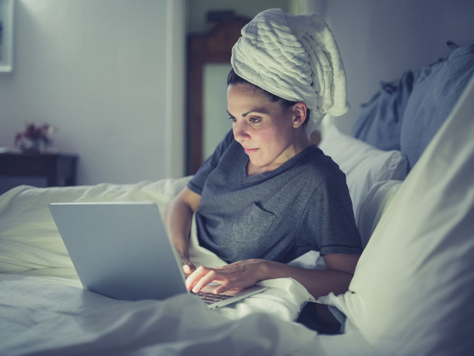 Frau am Laptop im Bett will mit nassen Haaren schlafen gehen