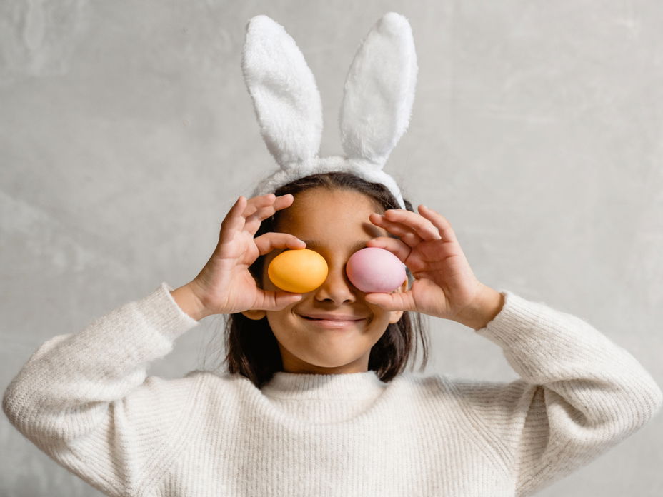 Kind mit Hasenohren hält sich zwei Ostereier vor die Augen