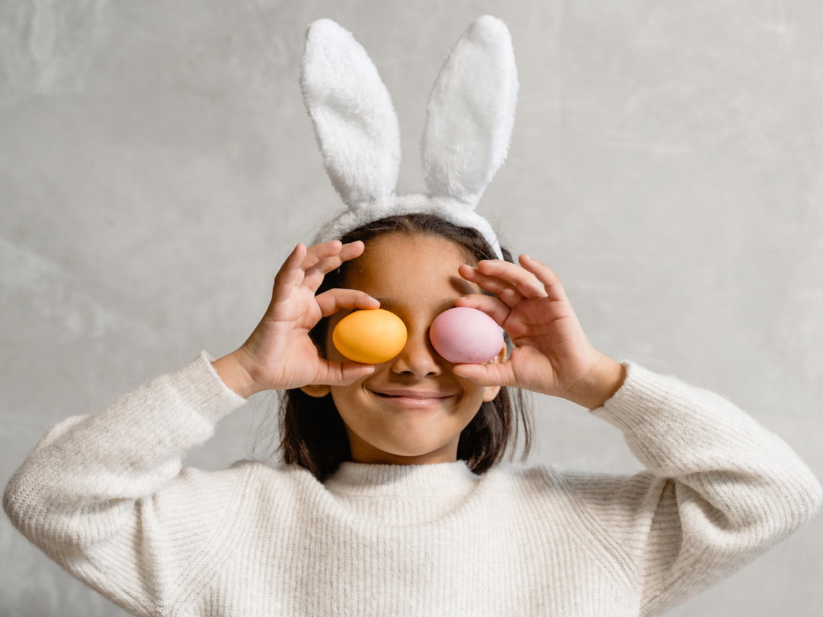 Kind mit Hasenohren hält sich zwei Ostereier vor die Augen