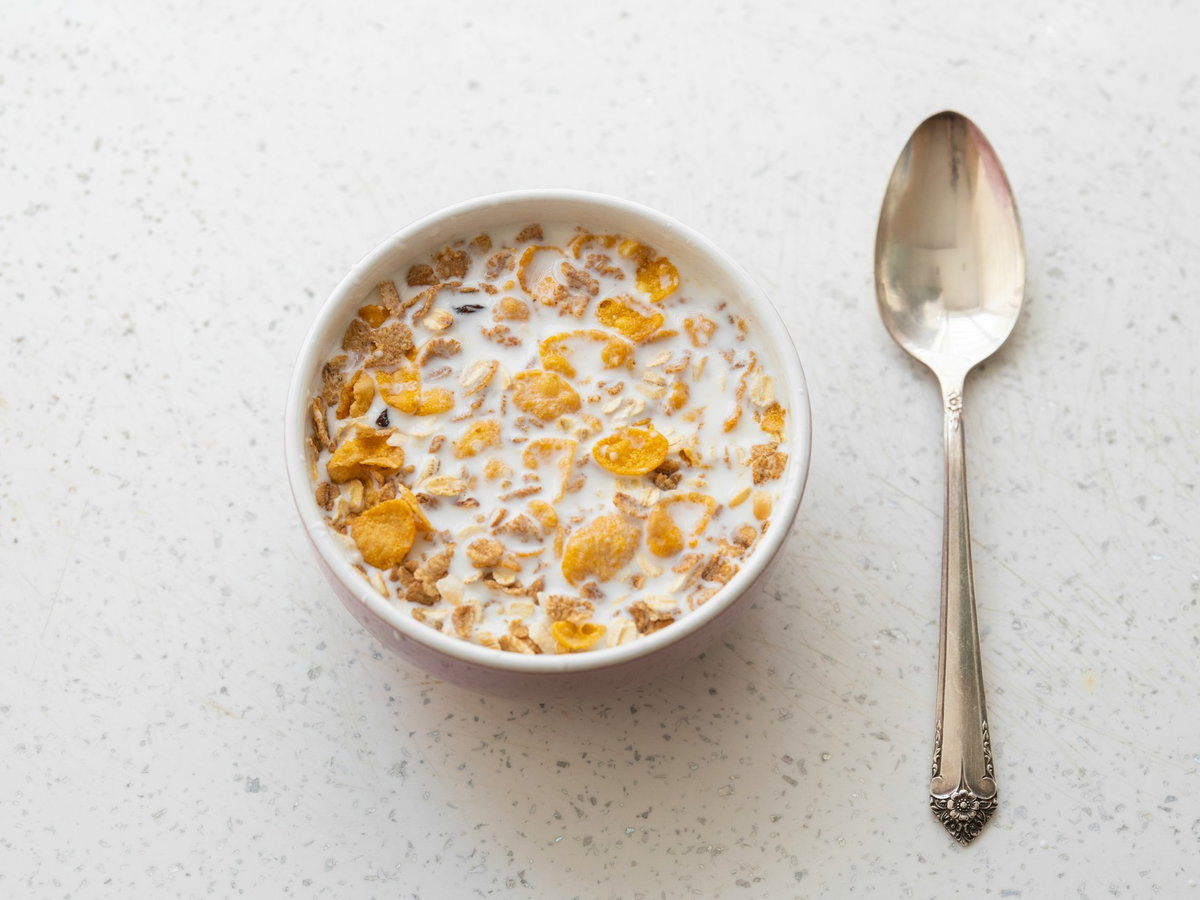 Cornflakes mit Milch in einer Schüssel mit einem Löffel daneben
