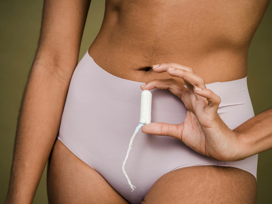 Frau hält einen Tampon vor ihrem Unterleib in der Hand.