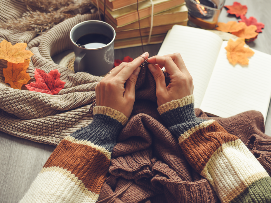 Frau strickt und hat ein Strickbuch parat