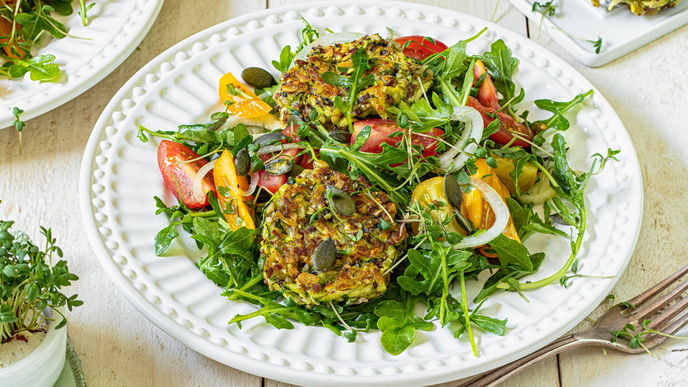 Die veganen Zucchini-Bratlinge werden auf einem Tomaten-Rucola-Salat serviert - und sind Low Carb!