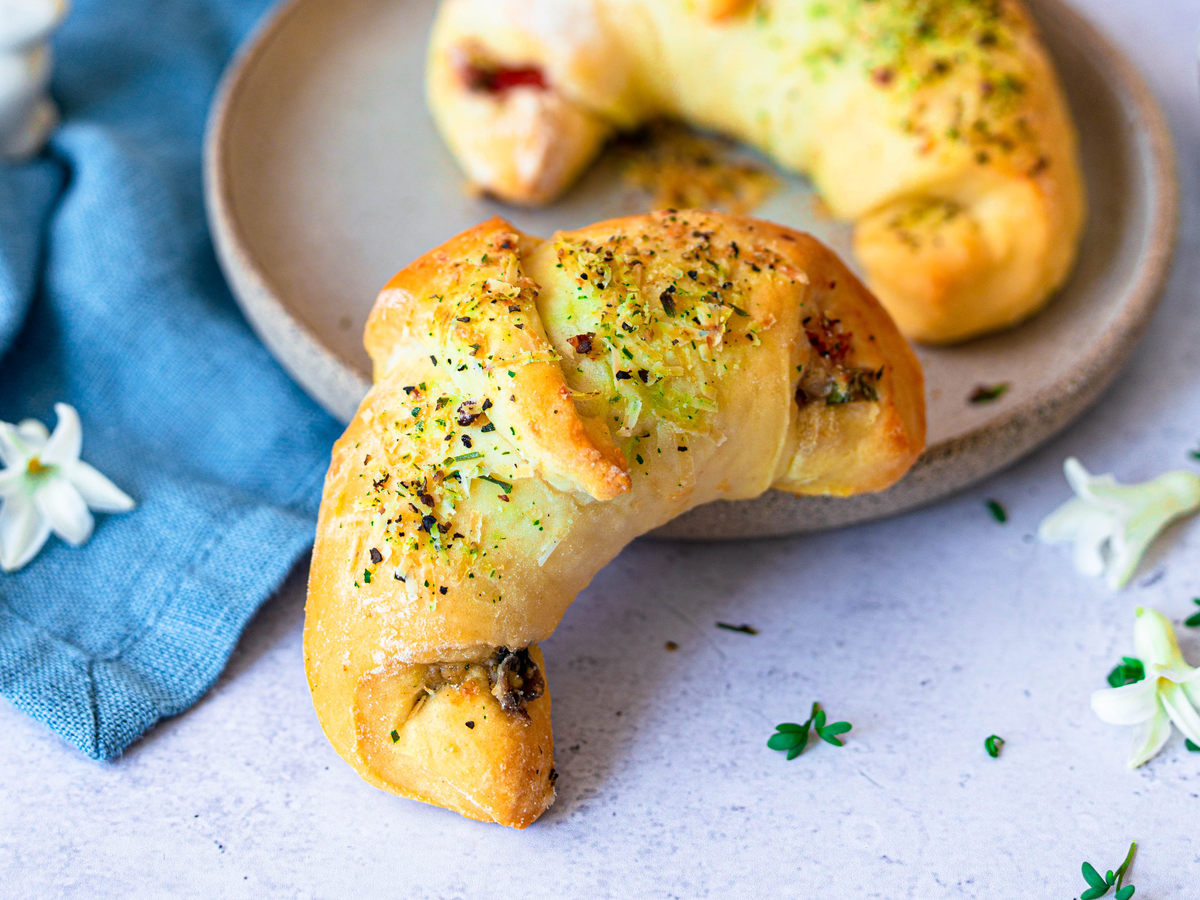 Pizzateig-Croissants mit Käse-Gewürz-Topping neben einem Teller angerichtet
