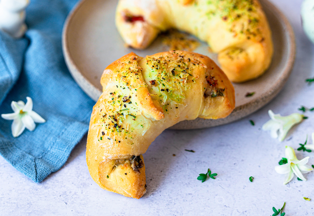 Pizzateig-Croissants mit Käse-Gewürz-Topping neben einem Teller angerichtet