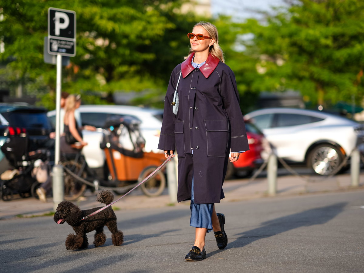 Eine blonde Frau, Mitte zwanzig, führt ihren Hund an einem sonnigen Frühlingstag in Kopenhagen durch die Straßen