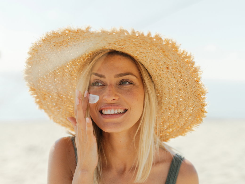 Frau mit Sonnenhut trägt Sonnencreme auf