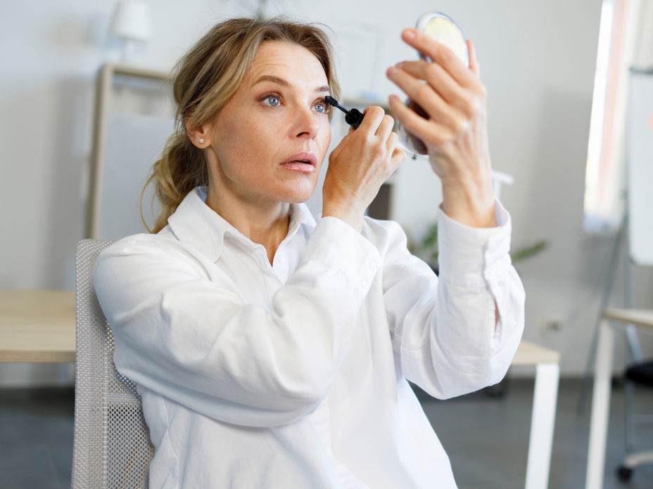 Frau tuscht Wimpern vor Handspiegel