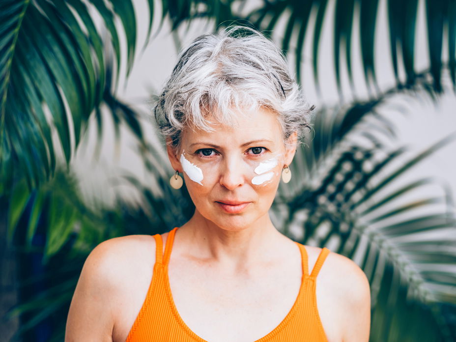 Frau mit grauen Haaren hat im Gesicht Sonnencreme aufgetragen