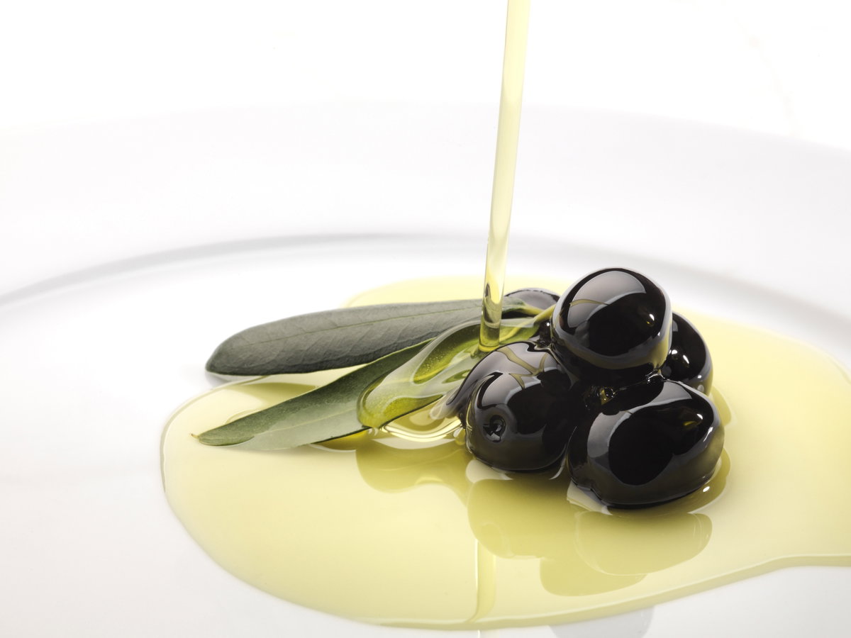 Schwarze Oliven werden mit Olivenöl übergossen - Vielseitig und gesund kochen mit Olivenöl