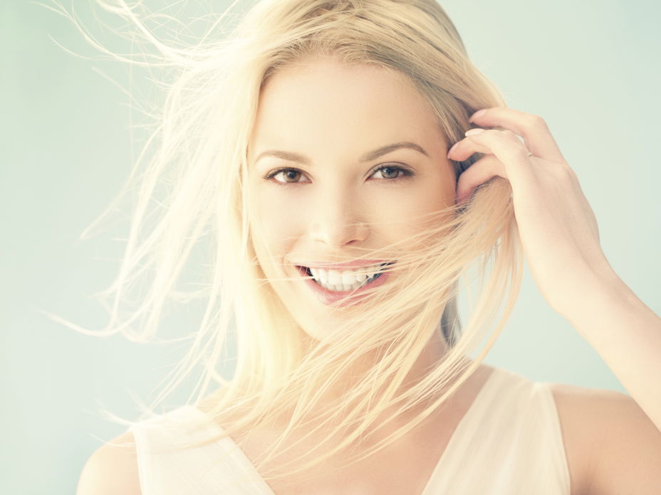 Eine Frau lächelt in die Kamera, ihre blonden Haare wehen im Wind
