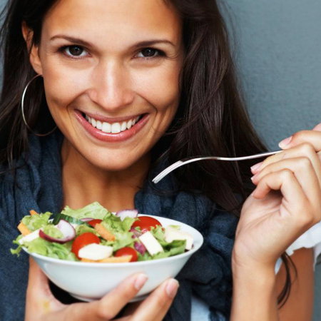 Dunkelhaarige, lachende Frau isst Salat
