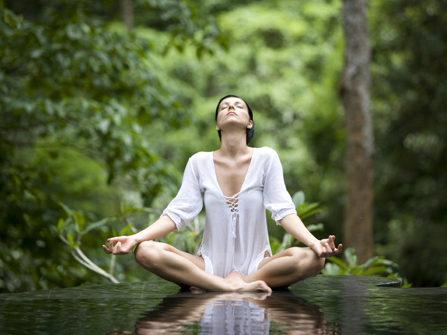 Eine Frau macht den Yoga Lotus-Sitz in einem grünen Wald