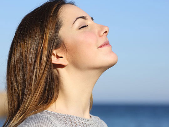 Eine Frau streckt das Gesicht der Sonne entgegen und atmet tief durch