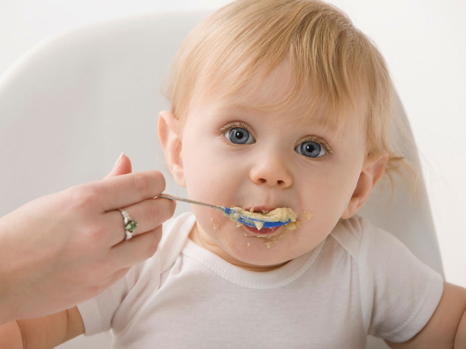 NIedliches blondes Baby wird mit Brei gefüttert