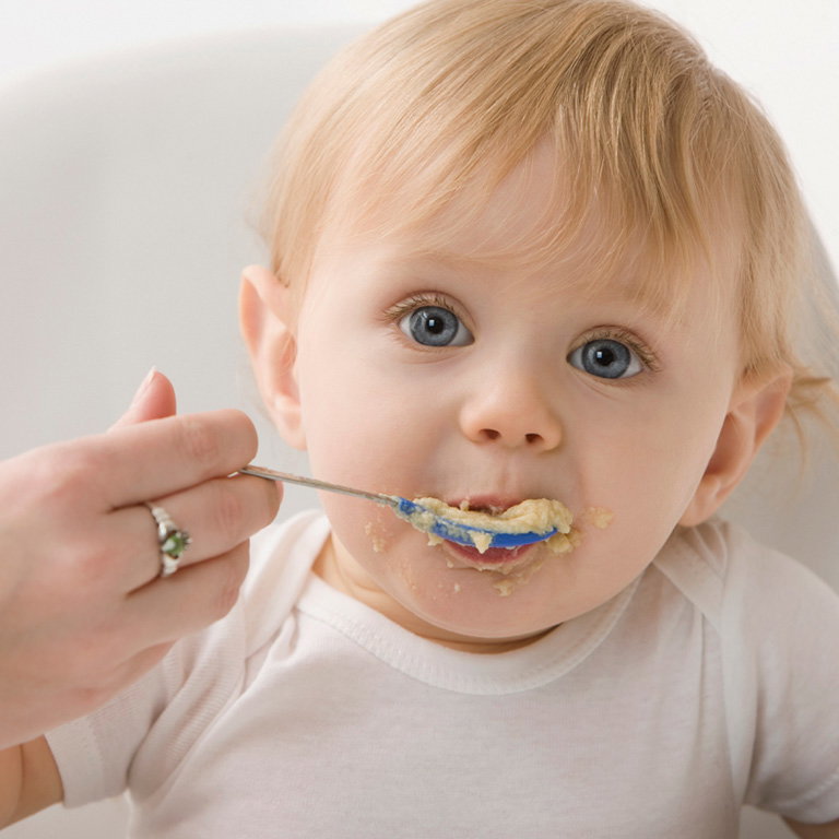 NIedliches blondes Baby wird mit Brei gefüttert