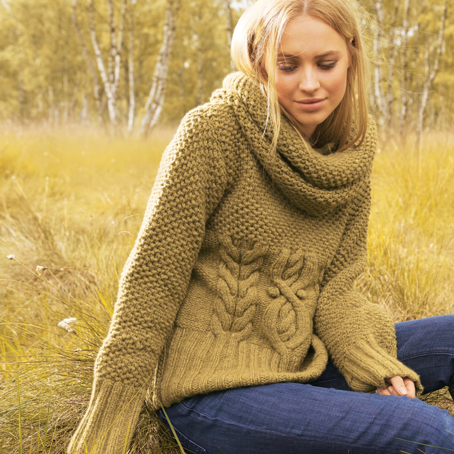 Blonde Frau trägt Strickpulli mit Zopfmuster und Loop im Olivton